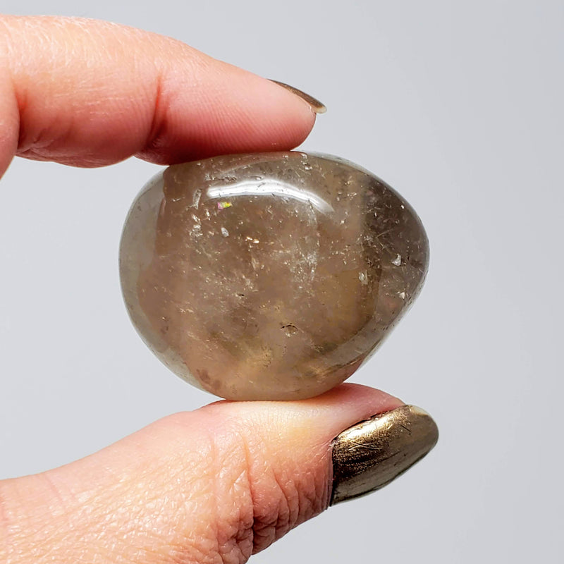 A hand holding up a tumbled Smokey Quartz on a white background