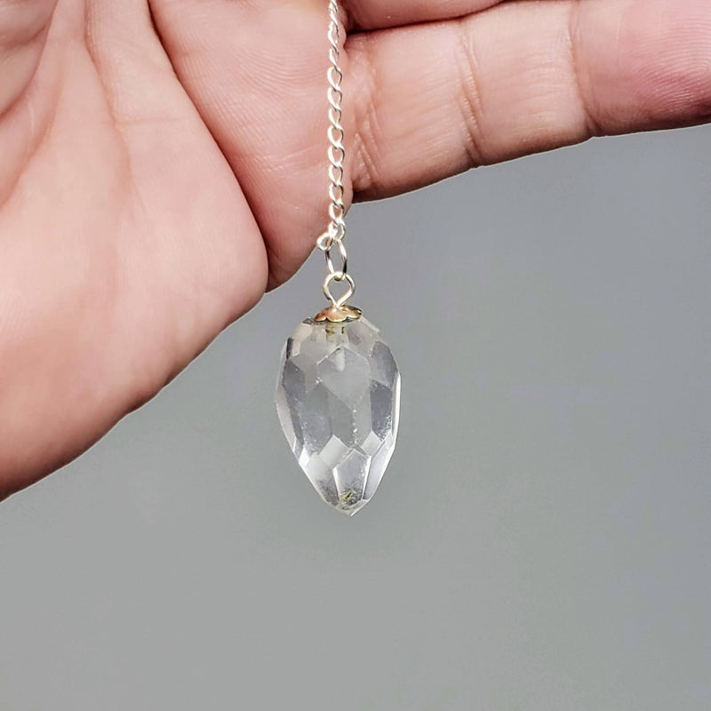 Close-up of Clear Quartz pendulum draped over a hand on a gray background.