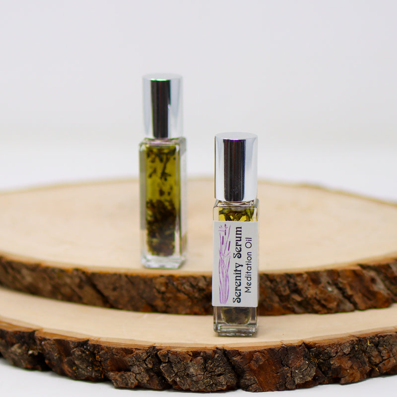 A front and back view of Serenity Serum Meditation Oil on top stacked natural wood slabs with a white background