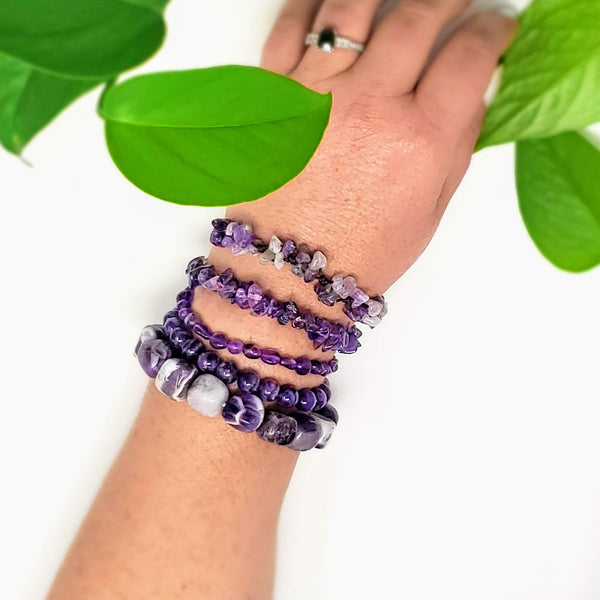 5 different styles of Amethyst bracelets adorn a wrist on a white background 