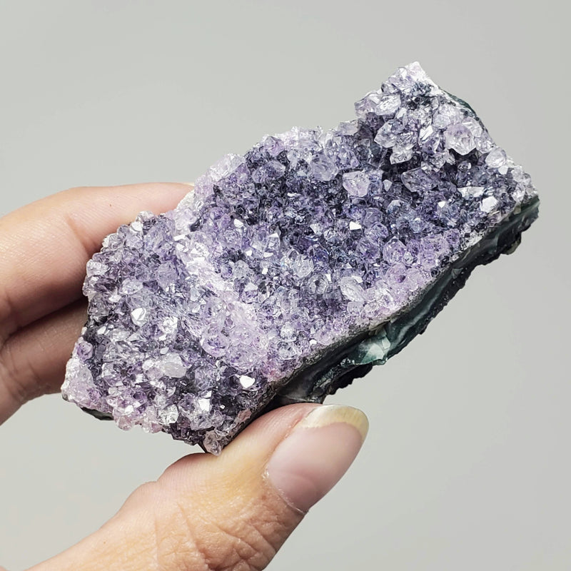 A hand holding up an Amethyst Cluster in front of a white background