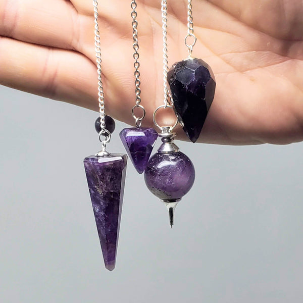 4 different styles of Amethyst pendulums gently draped over a hand on a white background
