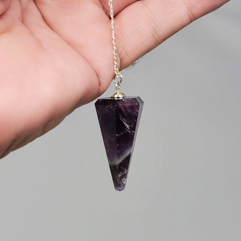 Amethyst Pendulum in hand with gray background