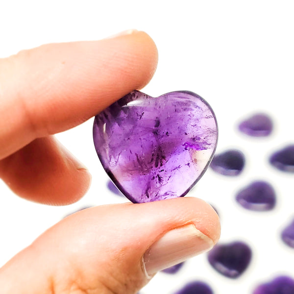 Close-up of an Amethyst Pocket Heart being held between forefinger and thumb, with more hearts scattered around in the background