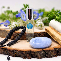 Our Bye-Bye Anxiety Meditation Set includes a Meditation scroll, Anxiety relief anointing oil, Blue Calcite palmstone, and Lava diffuser bracelet as shown here, displayed in front of fresh flowers. 