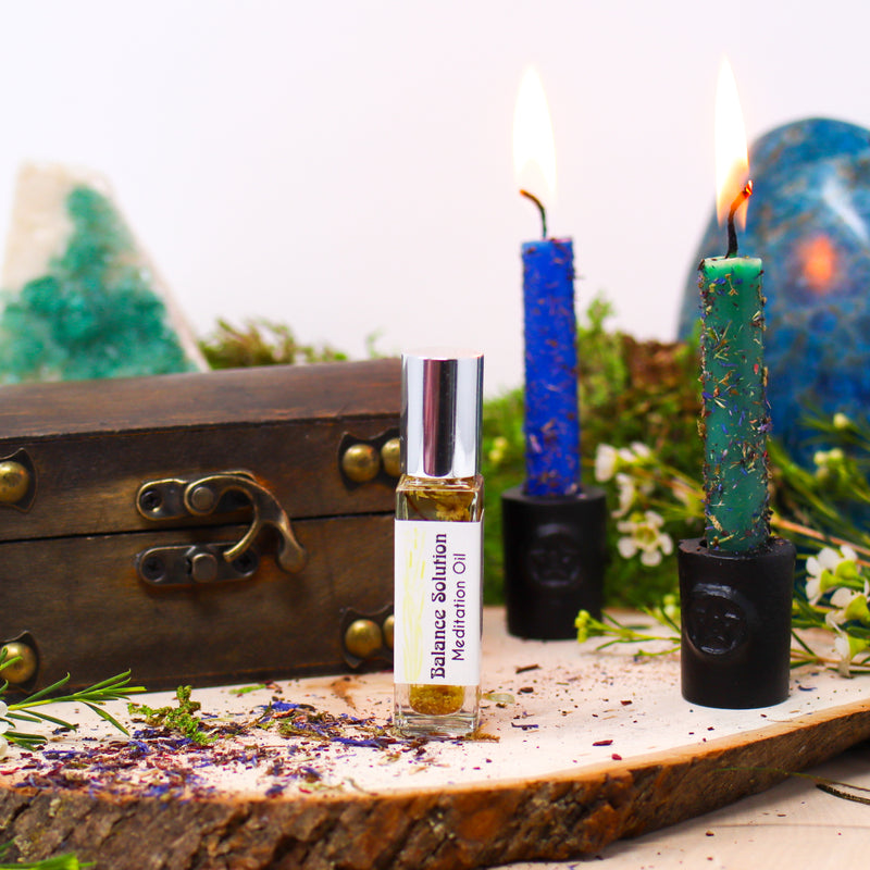 A bottle of Balance Solution Meditation Oil standing on a natural wood slab with a wooden box and two burning candles in the background 