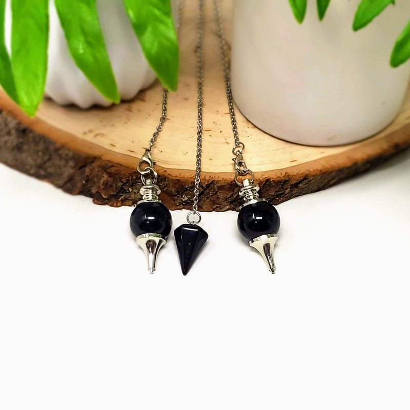 Different styles of Black Obsidian pendulums draped gently over a natural wood slab with a white background