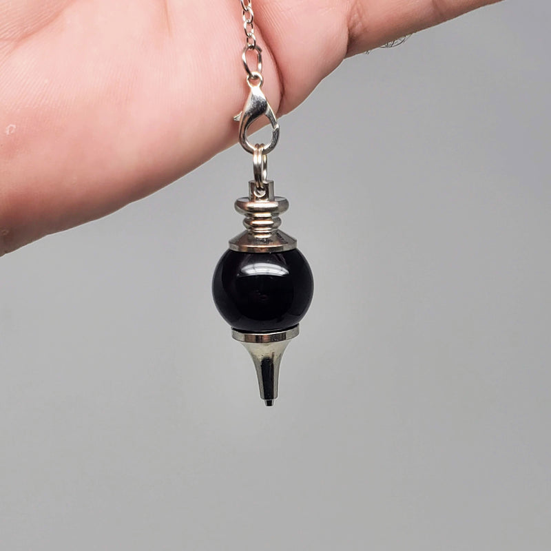 Black Obsidian pendulum draped over an open palm on a gray background