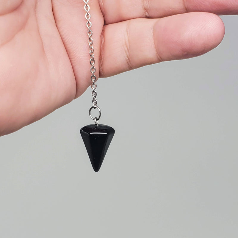 Black Obsidian pendulum draped over an open palm on a gray background