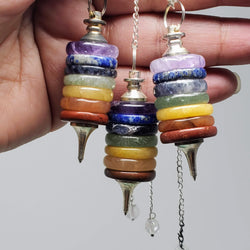 A close-up of 3 Chakra Button Stacked Pendulums draped over a hand on a white background