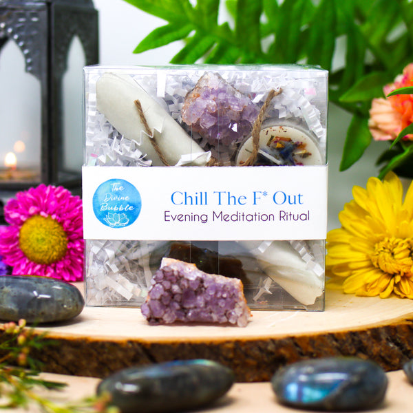 A beautiful display that features our Chill The F*ck Out Evening Meditation Ritual, surrounded by Labradorite palm stones, a Lavender Amethyst cluster, and brightly colored fresh flowers