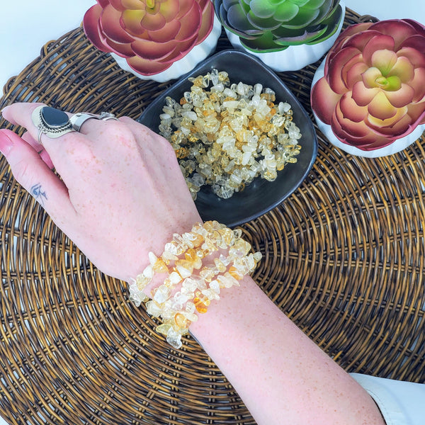 4 Citrine chip bead bracelets displayed on a wrist, next to a bowl full of more Citrine bracelets, all surrounded by potted succulents