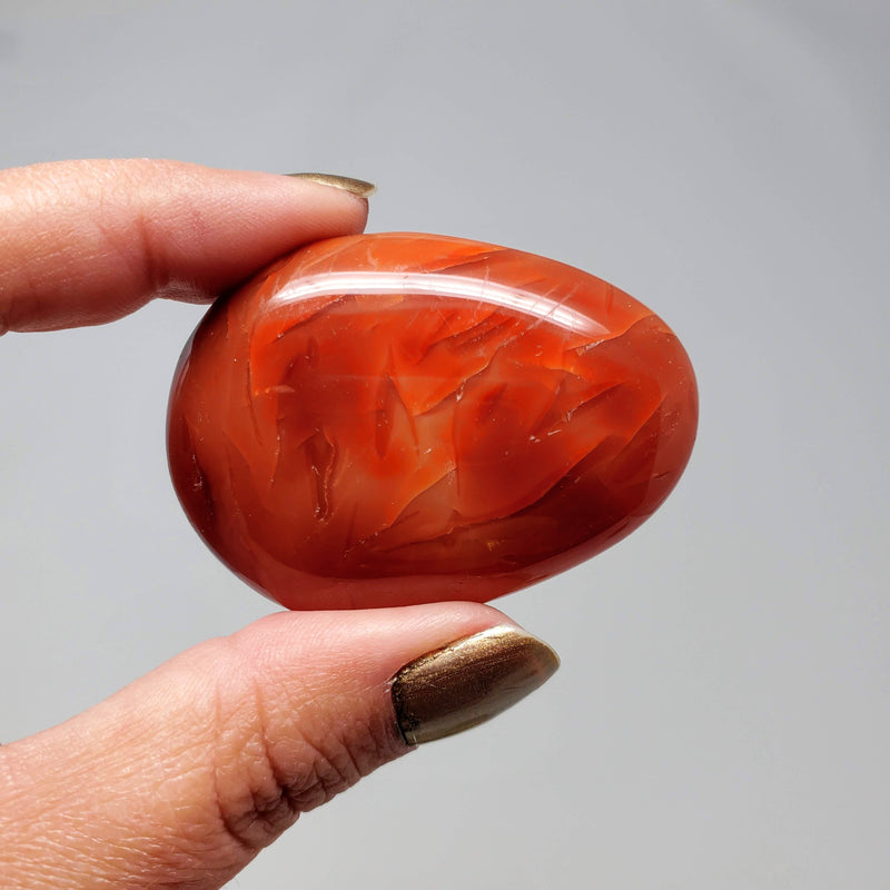 Carnelian Palm Stone held up between forefinger and thumb
