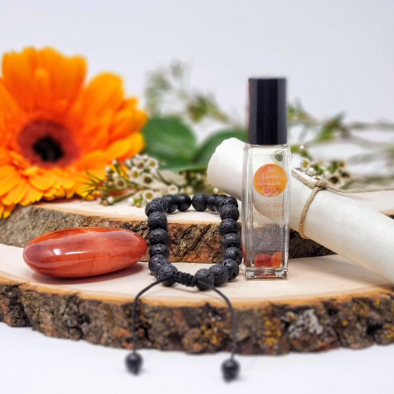 BE A BAD@SS MORNING MEDITATION RITUAL kit contents, including Courage Cocktail anointing oil, Carnelian palm stone, Lava and Onyx diffuser bracelet, and Meditation scroll, artistically arranged amongst flowers on natural wood slabs