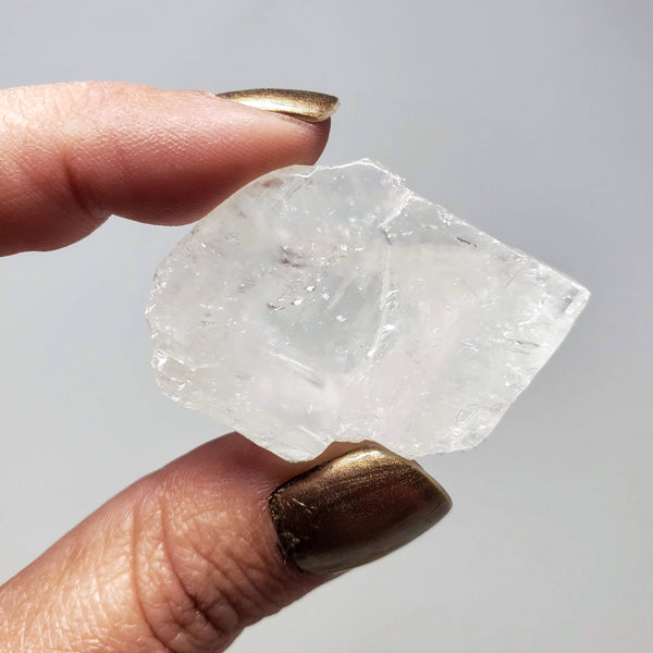 A hand holding up a raw White Calcite chunk on a white background