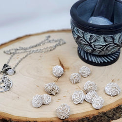 Several Desert Rose Selenite Baby Clusters on a natural wood slab, with a mortar and pestle, and Pentagram and Goddess necklace to add a little "witchy" flair