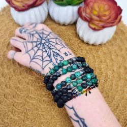 5 Emerald & Lava bracelets displayed on a wrist, with potted succulents in the background