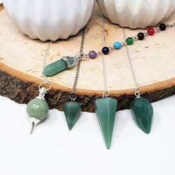 5 different styles of Green Aventurine pendulums displayed on a natural wood slab, on a white background