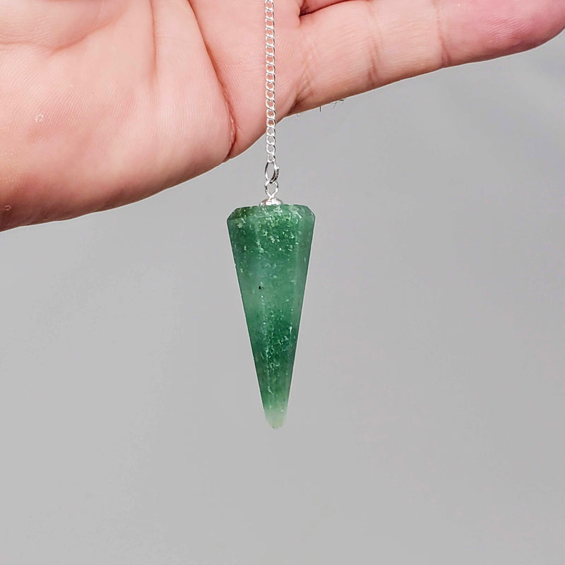 Green Aventurine pendulum draped over the palm of a hand on a gray background
