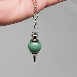 Green Aventurine pendulum draped over the palm of a hand on a gray background