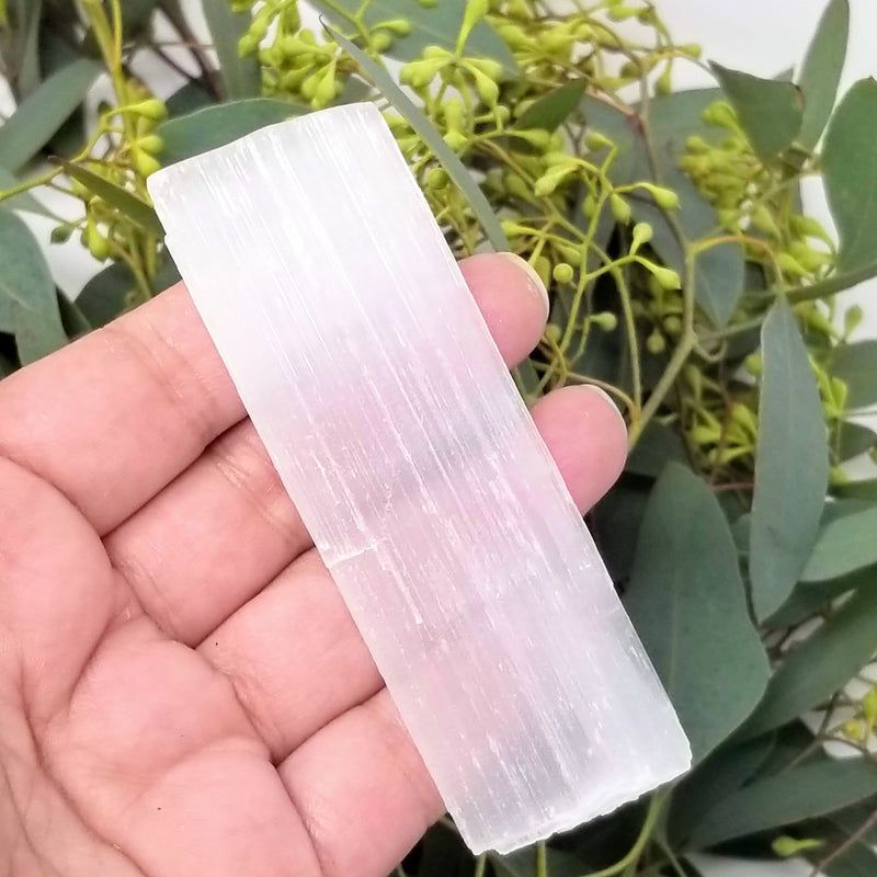 selenite stick in the palm of an open hand with greenery in the background