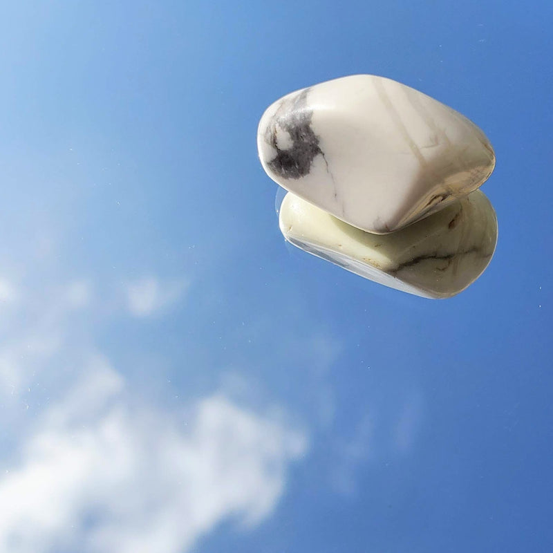 An artistic photo of a Howlite Tumbled Stone with the sky and clouds in the background 