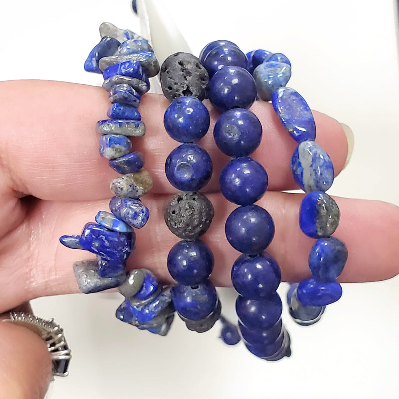 Close-up of 4 different styles of Lapis Lazuli Bracelets draped over two fingers with a white background