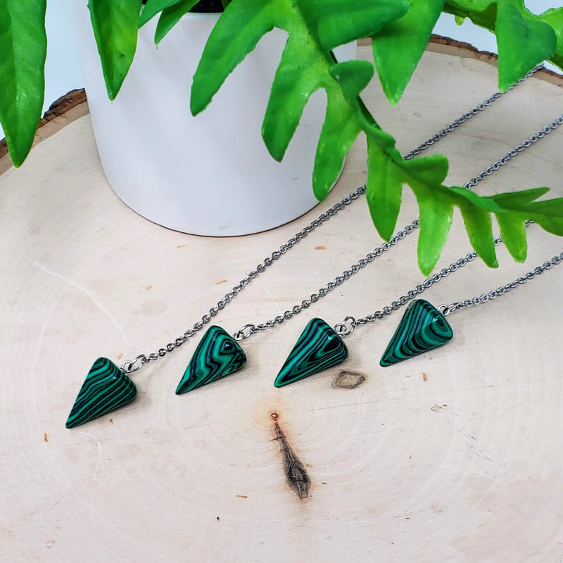 4 Malachite pendulums displayed on top of a natural wood slab with a plant in the background