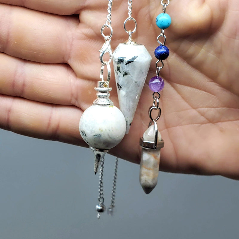 Moonstone Pendulums draped in a hand on a gray background 