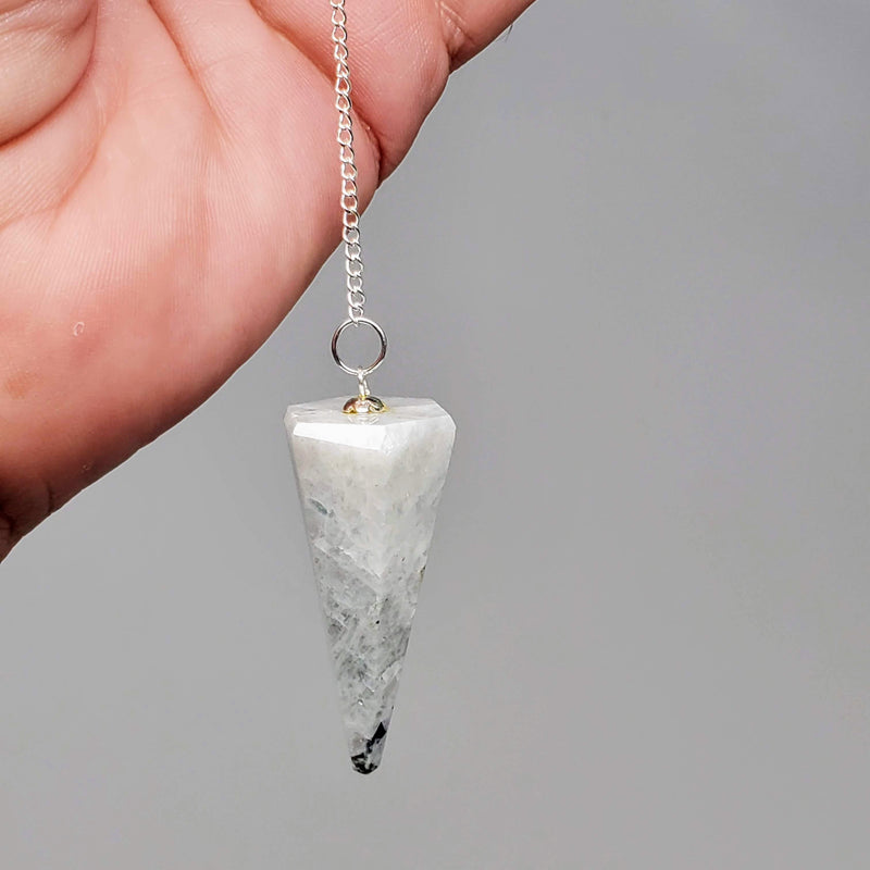 Moonstone Pendulum draped in a hand on a gray background 