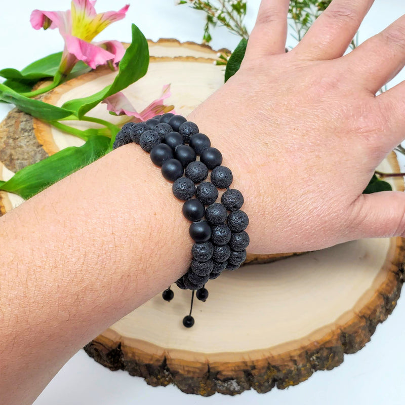 Three Lava and Black Onyx diffuser bracelets modeled on a wrist in front of fresh flowers
