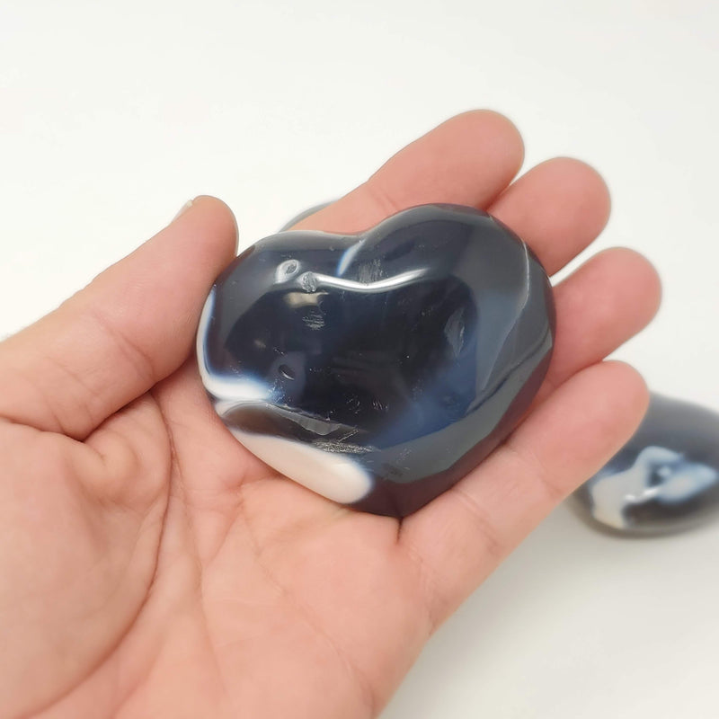 A hand holding up an Orca Agate Heart Palmstone