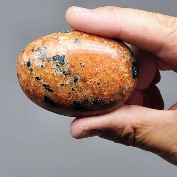 An Orchid Calcite palm stone held up between an forefinger and thumb in front of a white background