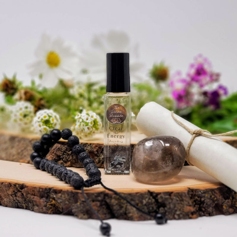The contents of our Bye-Bye Bad Juju Morning Meditation Ritual, including Lava and Black Onyx Diffuser Bracelet, Clear the Energy Anointing Oil, Smokey Quartz, and Meditation Script, all laid out on natural wood slabs with fresh flowers in the background