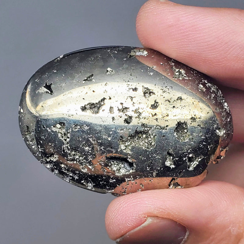 A Pyrite palmstone held up between a forefinger and thumb on a white background