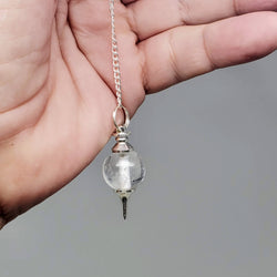 Close-up of Clear Quartz pendulum draped over a hand on a gray background.