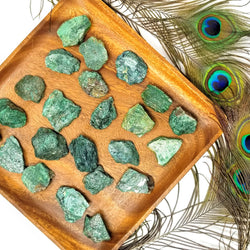 A wooden tray full of Raw Fuchsite surrounded by peacock feathers