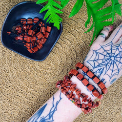 4 Red Jasper bracelets on a tattooed arm, with a bowl full of more bracelets to the side