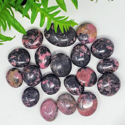 A variety of sizes of Rhodonite palm stones on a white background