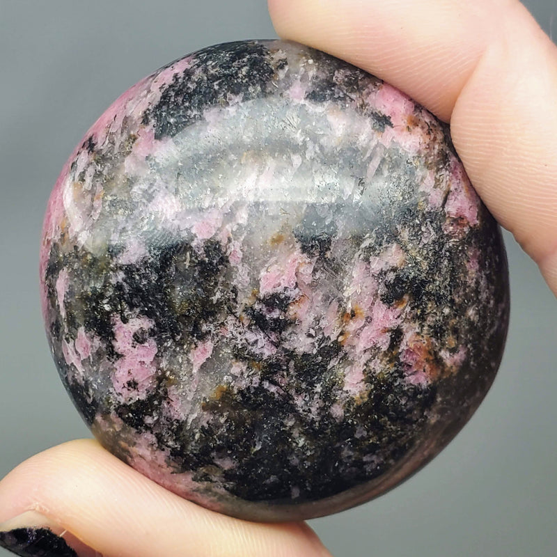 A close up view of a Rhodonite palmstone held between a forefinger and thumb