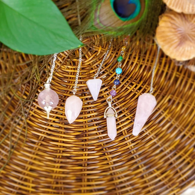 Five different styles of Rose Quartz Pendulums on wicker background.