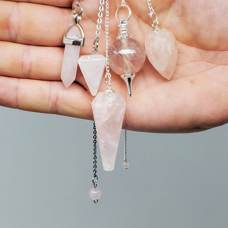 A variety of Rose Quartz Pendulums draped over hand on gray background. 