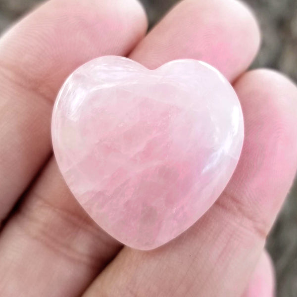 A close up of a Rose Quartz pocket heart resting on the fingers of an open hand