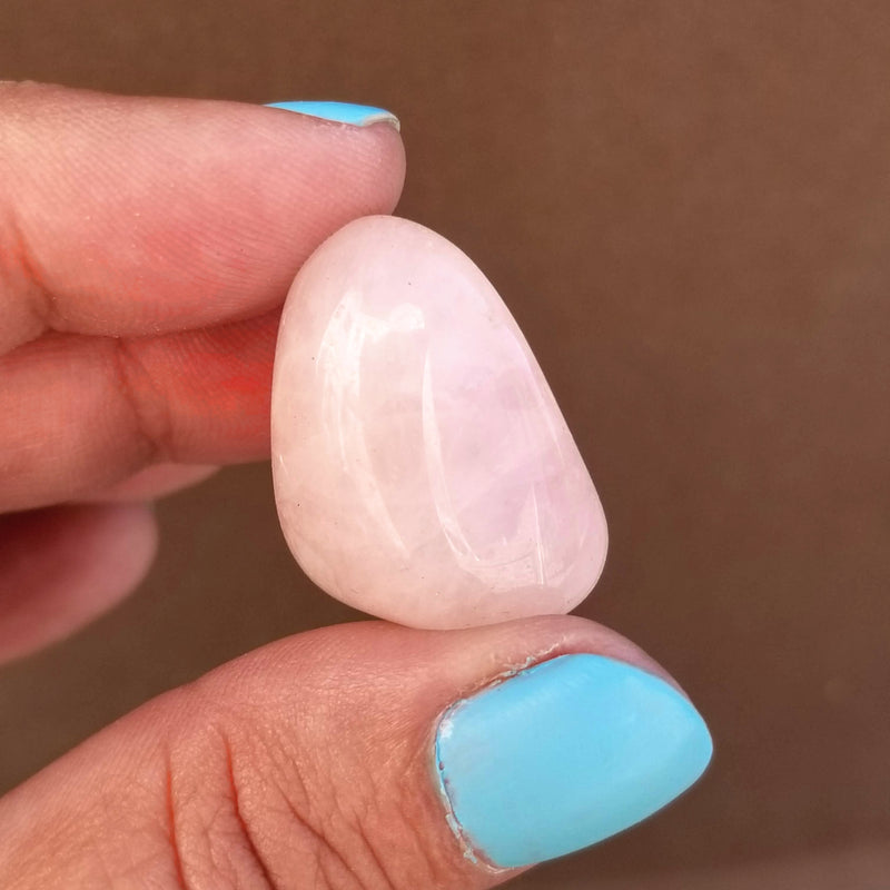 A Rose Quartz Tumbled Stone held up between a forefinger and thumb