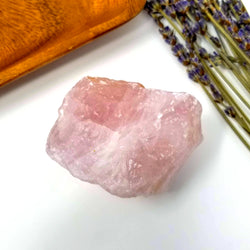 Rose Quartz Raw Chunk and purple flowers on a white background