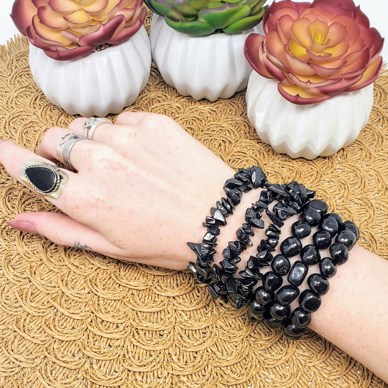 Different varieties of Shungite bracelets on a wrist, with potted succulents to the side
