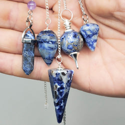 Sodalite Pendulums draped over a hand on gray background.