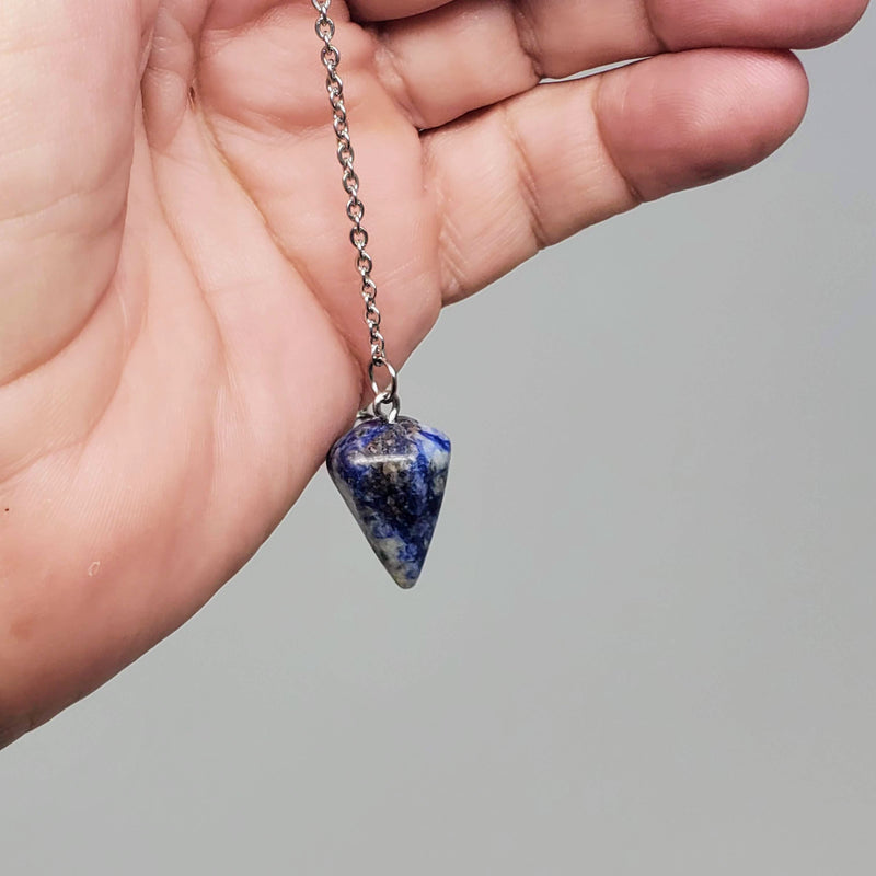 Sodalite Pendulum draped over a hand on gray background..