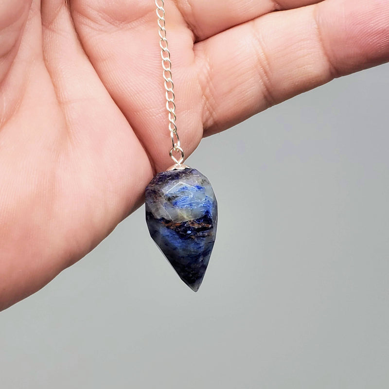 Sodalite Pendulums draped over a hand on gray background.