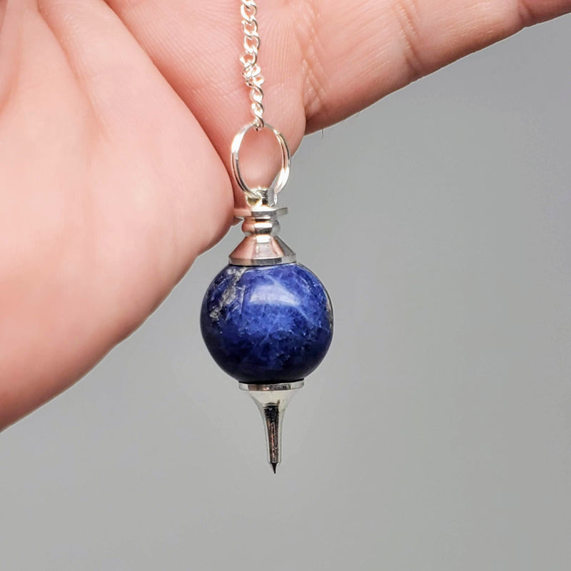 Sodalite Pendulums draped over a hand on gray background.